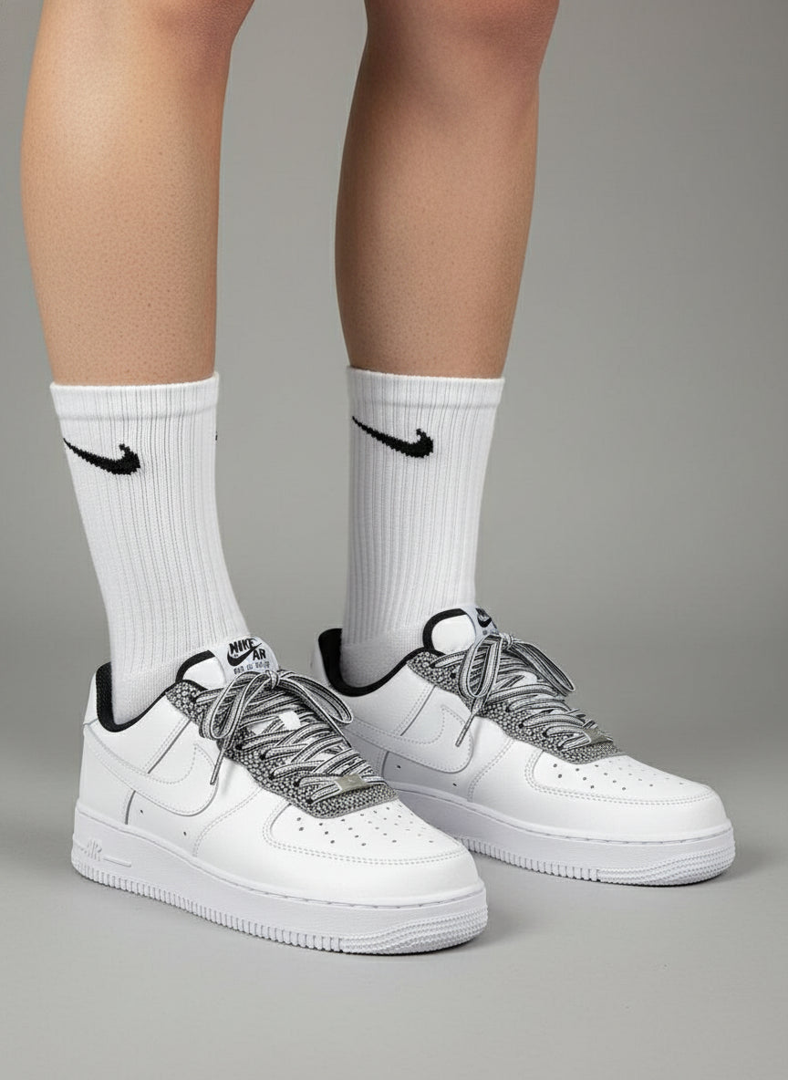White sneakers with black accents worn with white socks featuring a black logo on a gray background
